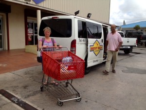 Birgit Pammé steht auf dem Parkplatz eines Supermarktes mit dem Einkaufswagen neben dem Shopping-Shuttle (ein Kleinbus)