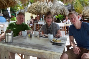 Teilnehmerin sitzt mit ihren Begleitern zum essen am Tisch unter Palmen und Sonnenschirm