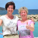 Karin Hirsch-Gerdes und Birgit Pammé stehen auf Curaçao vor dem Delphinbecken und halten die Daumen hoch
