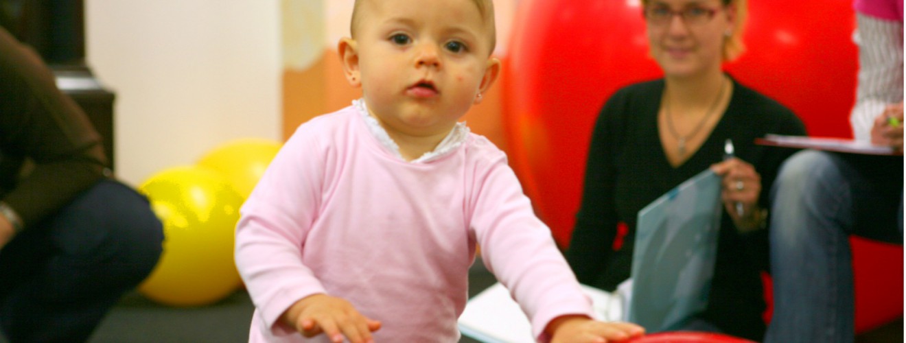 Das Kleinkind Louise spielt mit einem Therapieball und guckt herausfordernt in die Kamera